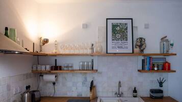 A kitchen with wooden shelves, a framed picture, and various kitchen items.