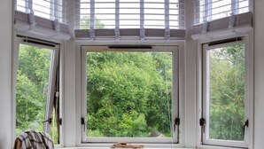 Ein Zimmer mit Erkerfenster und Blick auf ein bewaldetes Gebiet, ein Stuhl und ein kleiner Tisch.