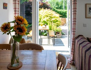 Comedor con una mesa, sillas, un jarrón con girasoles y vista a un jardín a través de puertas de vidrio.