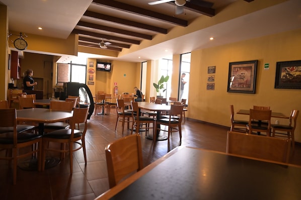 Un restaurante con mesas y sillas de madera, un reloj y cuadros en las paredes.