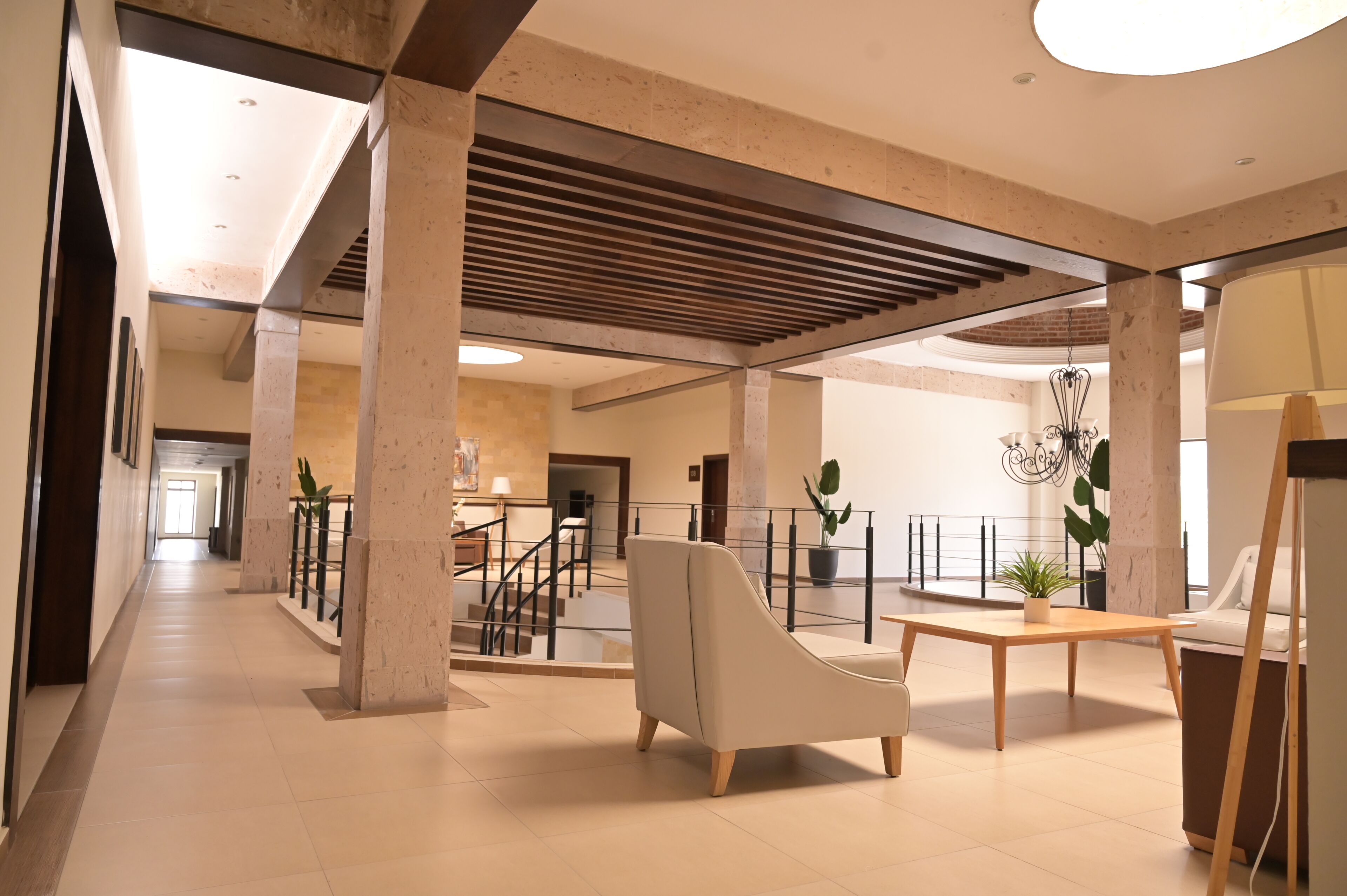A spacious lobby with a modern design, featuring a central seating area, a staircase, and a view of the upper floor.