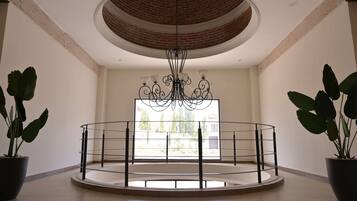 A spacious room with a circular railing, a large window, and a chandelier.