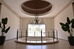 Una habitación amplia con barandilla circular, un ventanal grande y un candelabro.