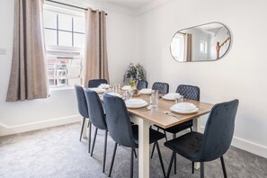 A dining area with a table set for four, a mirror on the wall, and a window with curtains. - Luxe 4-bedroom house perfect for groups | great transport links! (London)