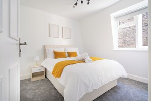 Une chambre à coucher avec un lit, une table de chevet, une fenêtre ornée d’un motif en briques et une porte.