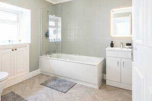 A bathroom with a bathtub, a toilet, a sink, and a mirror. - Luxe 4-bedroom house perfect for groups | great transport links! (London)