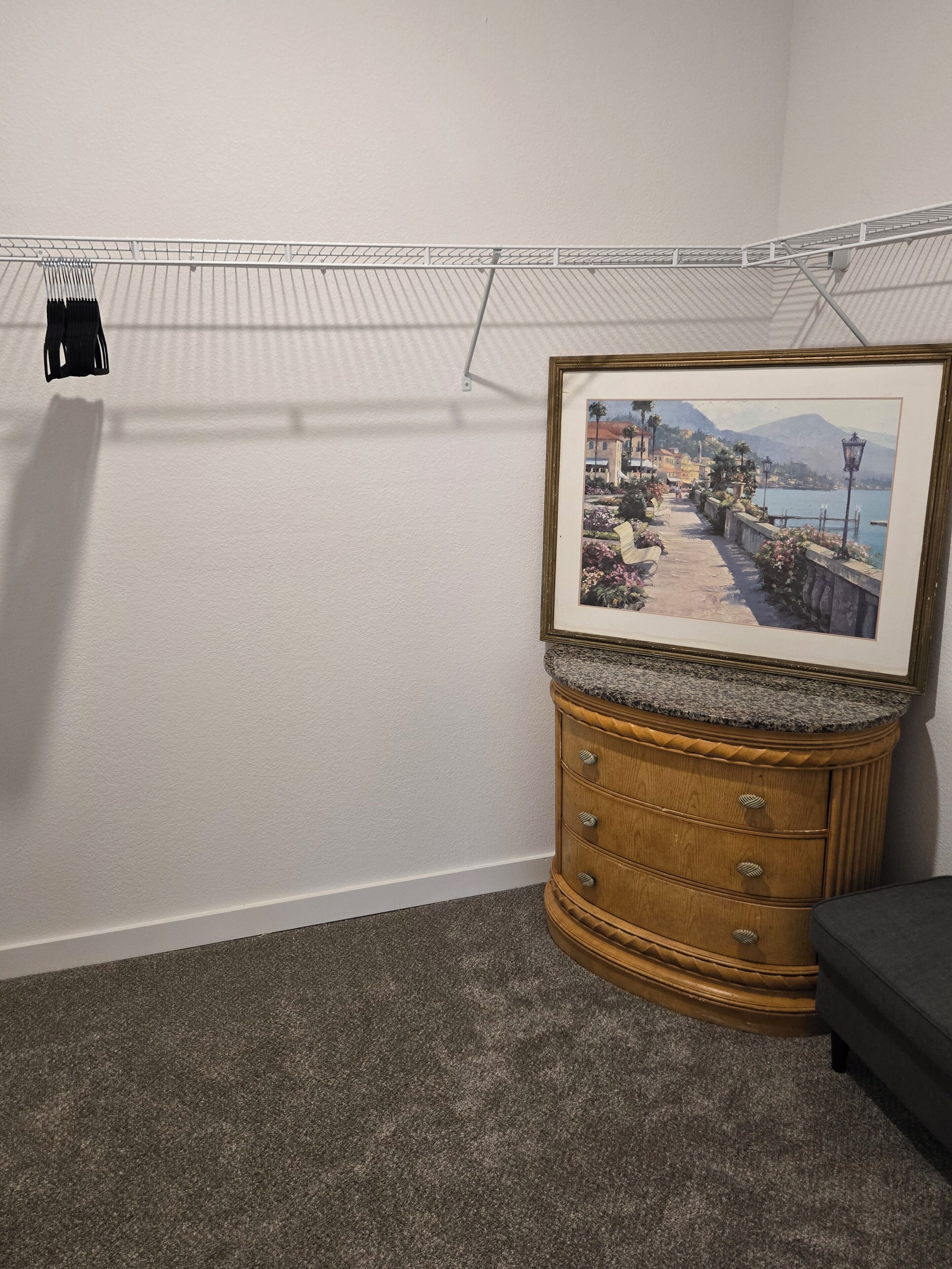 Ein Zimmer mit einem Bilderrahmen, der eine Küstenansicht zeigt, einer Holzkommode und einem Kleiderhaken.