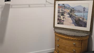 Une pièce comprenant un tableau encadré représentant un paysage côtier, une commode en bois et un porte-manteau suspendu.