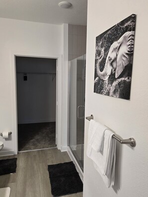 A bathroom with a shower, a toilet, a sink, a towel rack, and a picture of an elephant.