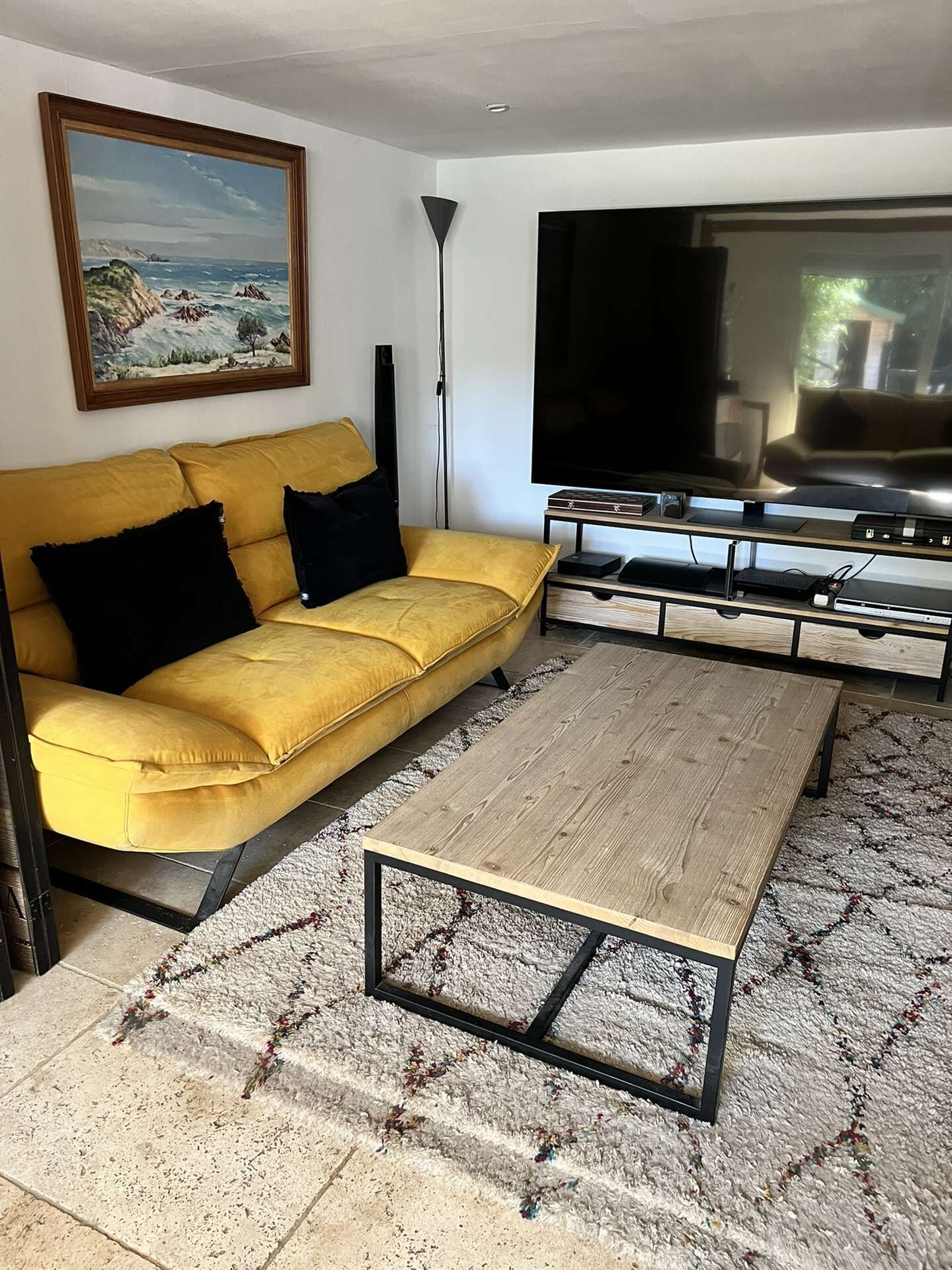 Una sala de estar con un sofá amarillo, una mesa de centro, un televisor de pantalla plana y un cuadro en la pared.