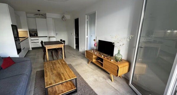Ein modernes Wohnzimmer mit Sofa, Couchtisch, TV-Schrank und einem Essbereich mit Stühlen und Tisch.