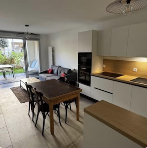 A modern kitchen with white cabinets, a dining table with chairs, and a sofa with red cushions. - Rez-de-jardin 4 couchages (SIX FOURS LES PLAGES)