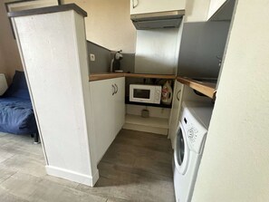 Una kitchenette compacta con microondas, lavadora y un pequeño armario.