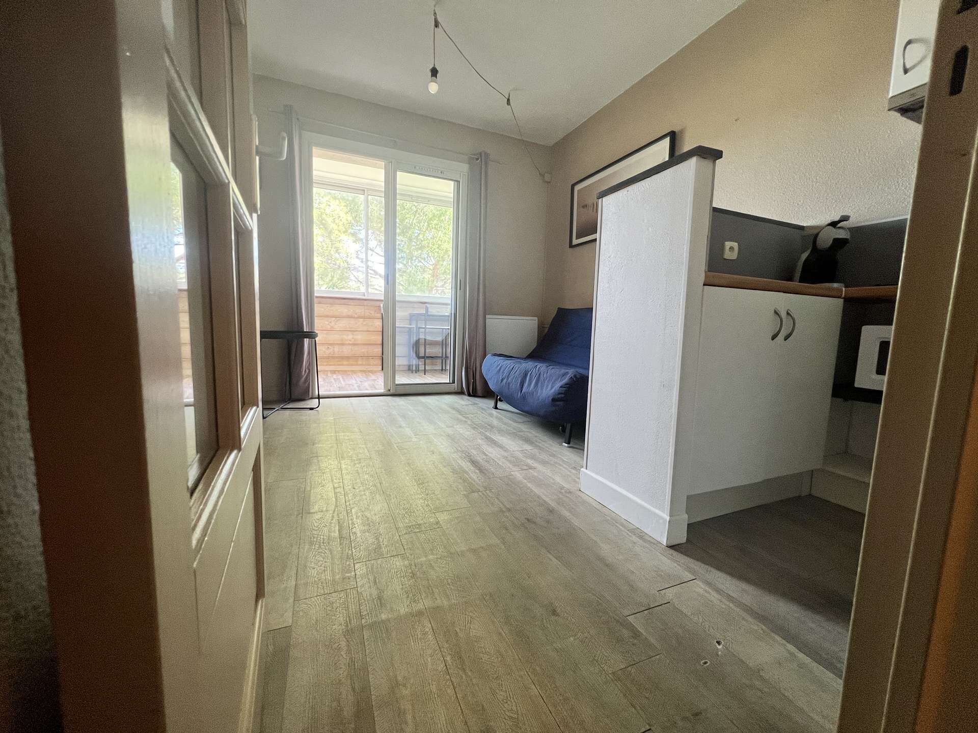 Une pièce compacte comprenant un coin cuisine, un lit et une porte-fenêtre coulissante donnant sur un espace extérieur.