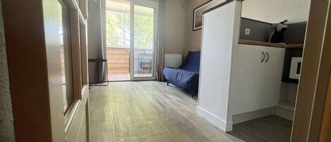 A compact room with a kitchenette, a bed, and a sliding glass door leading to an outdoor area.