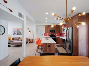 A modern kitchen with a central island, a dining area with orange chairs, and a living space with a sofa and a painting. - Desert Dream - Pool Heat Avail. - Mins to Old Town (Scottsdale)