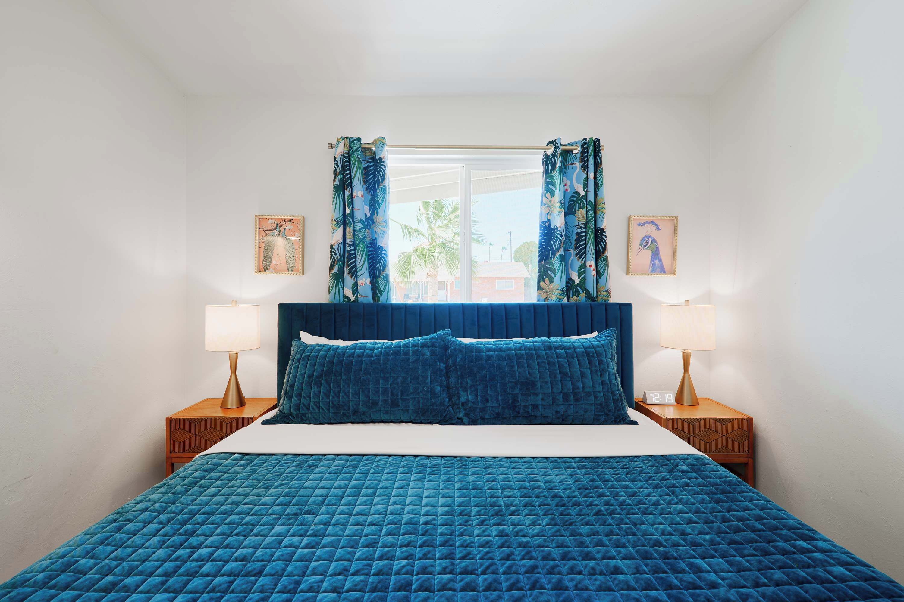 Een slaapkamer met een groot bed, twee nachtkastjes met lampen en twee ingelijste foto’s aan de muur.