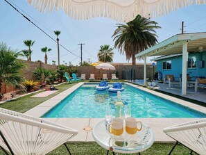 A swimming pool with lounge chairs and umbrellas, surrounded by palm trees and a blue house. - Desert Dream - Pool Heat Avail. - Mins to Old Town (Scottsdale)