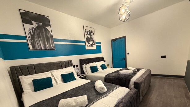 Ett hotellrum med två sängar, en blå dörr och konstverk på väggarna.