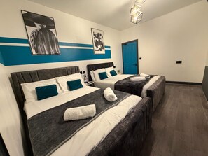 A hotel room with two beds, a blue door, and artwork on the walls. - Tudors eSuites - Modern Apartment (Birmingham)