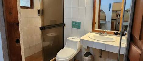 Un baño con cabina de ducha de vidrio, inodoro, lavamanos con espejo y suelo de baldosas.