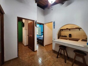 A narrow hallway leading to a kitchen with a white countertop and stools.