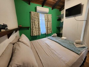 A room with a bed, a flat-screen TV, an air conditioner, and a window with curtains.