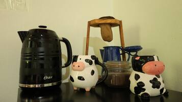 A black coffee maker, two ceramic pig-shaped mugs, a blue mug, and a wooden chair on a table.