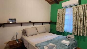 Un dormitorio con cama, mesita de noche, aire acondicionado, ventana con cortinas y ventilador de techo.