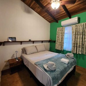 Quarto com cama, mesa de cabeceira, ar condicionado, janela com cortinas e ventilador de teto.