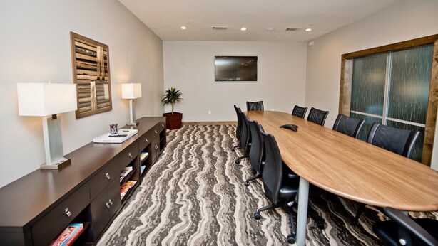 A conference room with a long table, chairs, a desk with a lamp, a potted plant, and a painting on the wall. - Accessible 1BR Suite w/ Free Hot Breakfast + Pool (Humble)