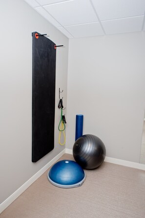 A small, private room with a black exercise wall, a blue exercise ball, and a yoga mat.