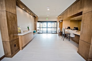 A modern hotel lobby with a reception desk, seating area, and a view of the outside.