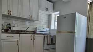 A kitchen with white cabinets, a white refrigerator, a stove, and a window. - Newly renovated suite, centrally located with full kitchen (Toronto)