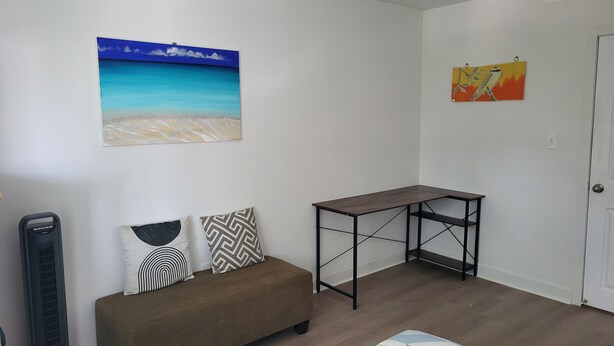 A room with a sofa, a standing fan, a table, and two wall-mounted artworks. - Newly renovated suite, centrally located with full kitchen (Toronto)