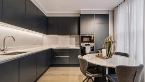 Uma cozinha moderna com armários escuros, bancada branca e área de refeições com mesa e cadeiras redondas.