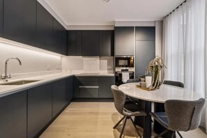 Eine moderne Küche mit dunklen Schränken, einer weißen Arbeitsplatte und einem Essbereich mit rundem Tisch und Stühlen.