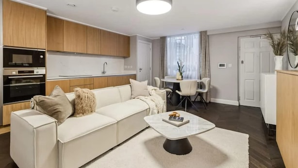 Una sala de estar moderna con un sofá, una mesa de centro y una cocina con armarios de madera y electrodomésticos.