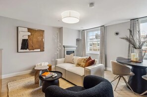 Ein modernes Wohnzimmer mit Sofa, Couchtisch, Beistelltisch, Sessel und einem Essbereich mit Tisch und Stühlen.
