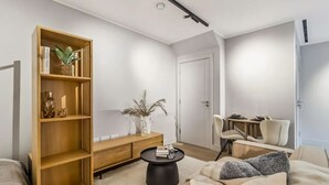 A modern living room with a wooden bookshelf, a round coffee table, a sofa, and a dining area with chairs. - 9 Mins Walk to Selfridges Marble Arch Studio (London)