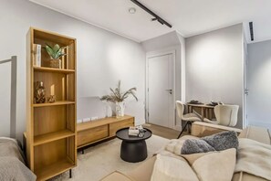 Ein modernes Wohnzimmer mit einer Holzbücherreol, einem runden Couchtisch, einer Couch und einem Essbereich mit Stühlen.