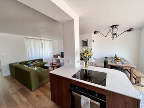 Et moderne køkken med en central ø, et spiseområde med et træbord, og en grøn sofa i en opholdsstue.