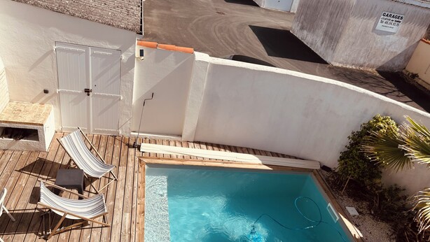 Una piscina en la azotea con terraza de madera, dos sillones reclinables a rayas y una mesita.