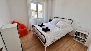 Un dormitorio con cama, ventana, radiador, estantería y una silla.
