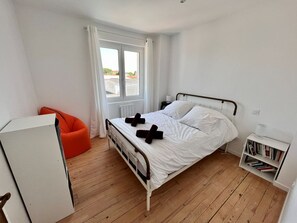 A bedroom with a bed, a window, a radiator, a bookshelf, and a chair. - Superbe villa avec piscine à 10 min du centre (La Rochelle)