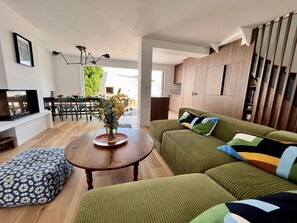A modern living room with a green sofa, a wooden dining table, and a kitchen area. - Superbe villa avec piscine à 10 min du centre (La Rochelle)
