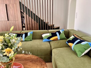 A green sofa with colorful pillows, a wooden coffee table, and a staircase in the background. - Superbe villa avec piscine à 10 min du centre (La Rochelle)