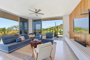 A modern living room with a sectional sofa, a coffee table, and a flat-screen TV mounted on the wall. - Hilltop Villa: Infinity Pool & Ocean Horizon (Playa Grande)