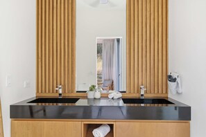 A bathroom with a black countertop, wooden cabinets, a large mirror, and a towel rack. - Hilltop Villa: Infinity Pool & Ocean Horizon (Playa Grande)