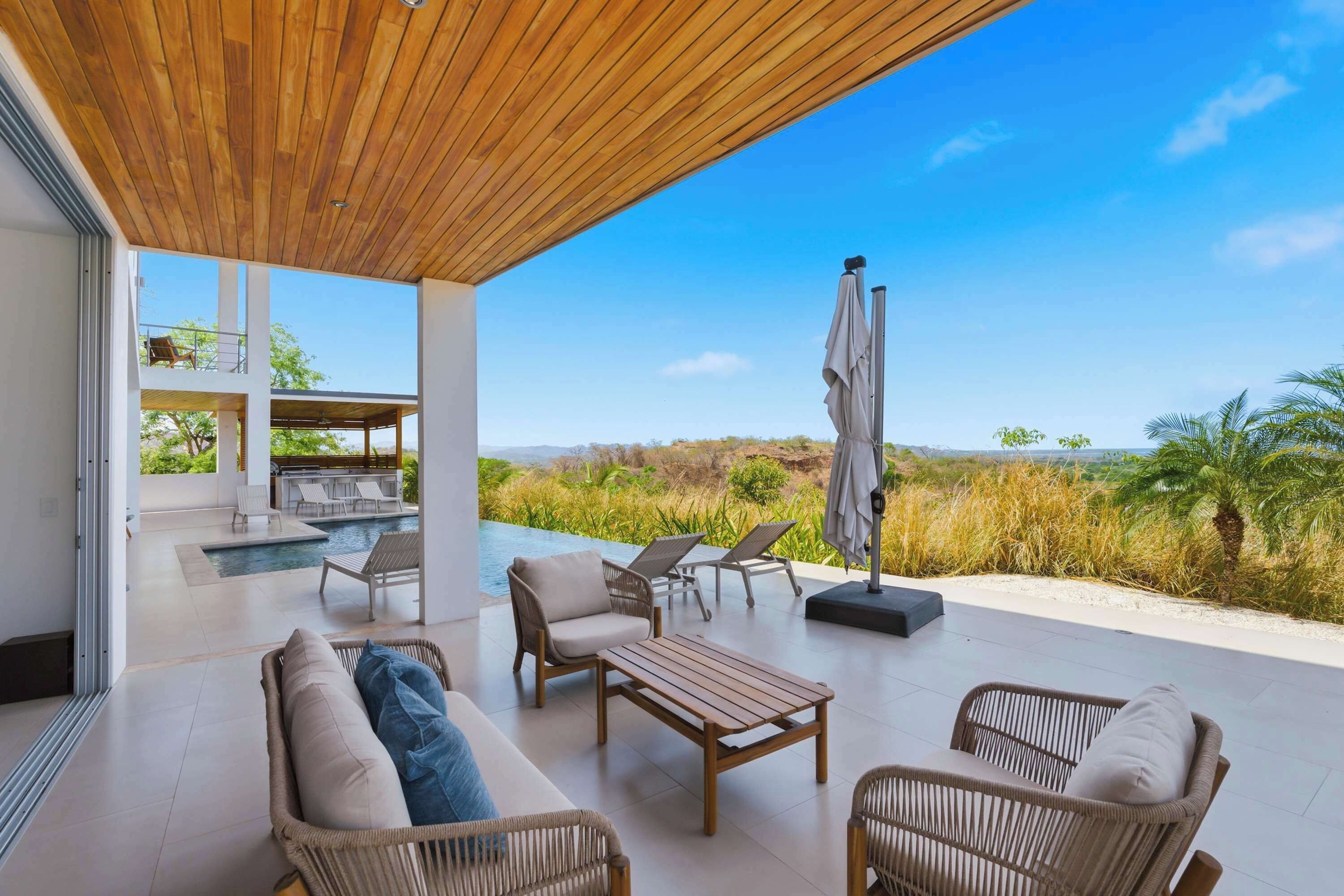 Une terrasse extérieure aménagée avec des meubles en osier, une piscine et une vue sur le paysage.
